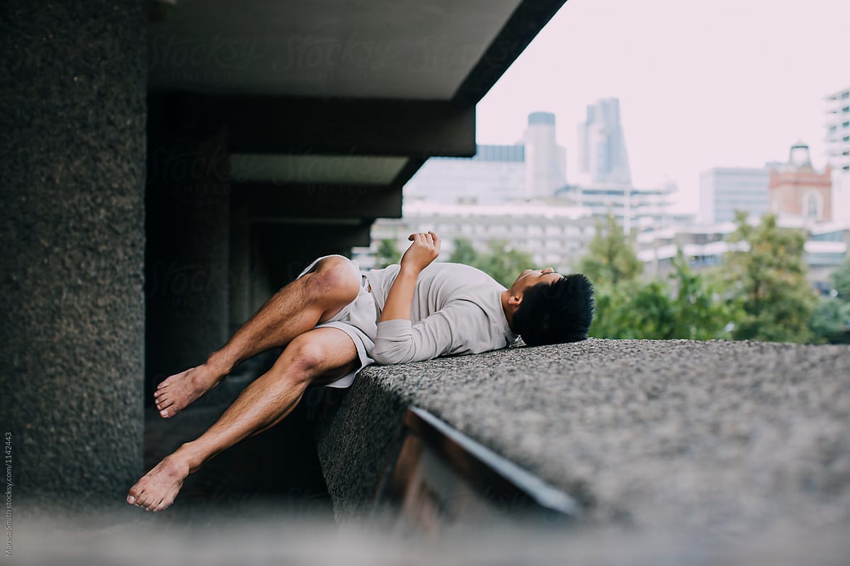 An Asian man lying on his back on a concrete ledge with the city in the distance