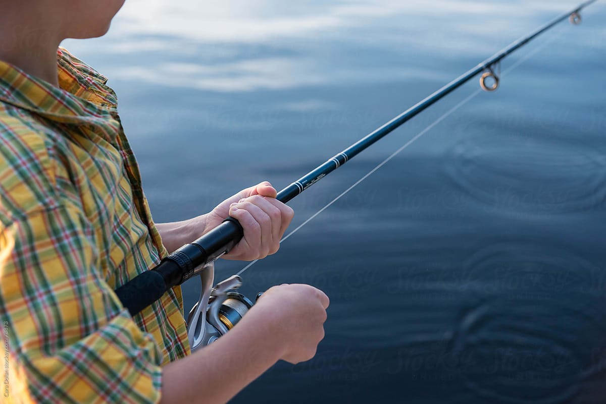 Boy reels in the line on his fishing pole at the lake