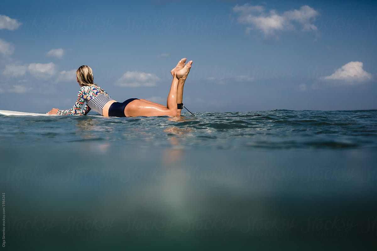 Young woman in swimsuit lying on surf board in the ocean.