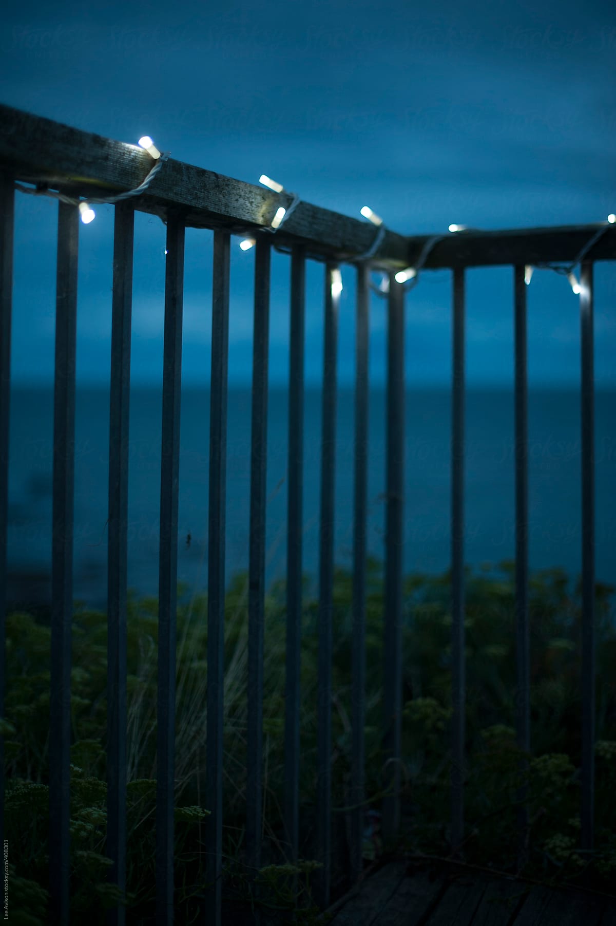 fence with fairylights by the sea at night