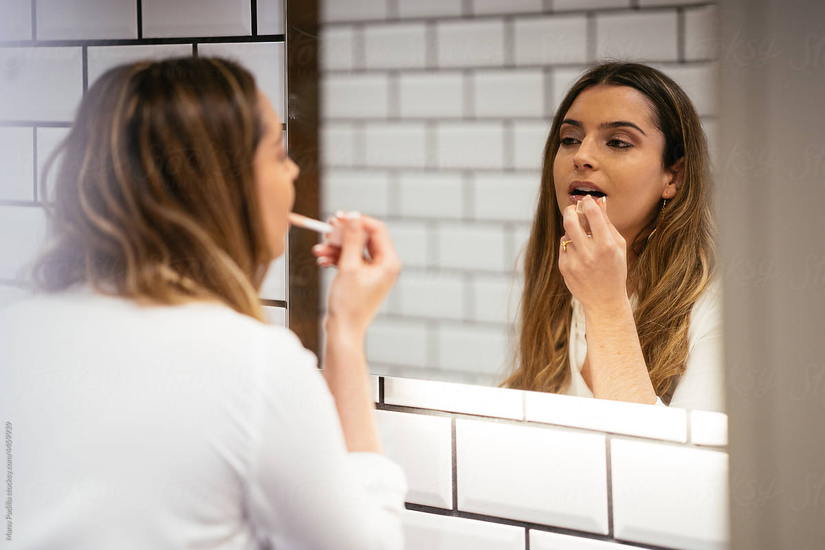 Woman applying makeup and looking in mirror