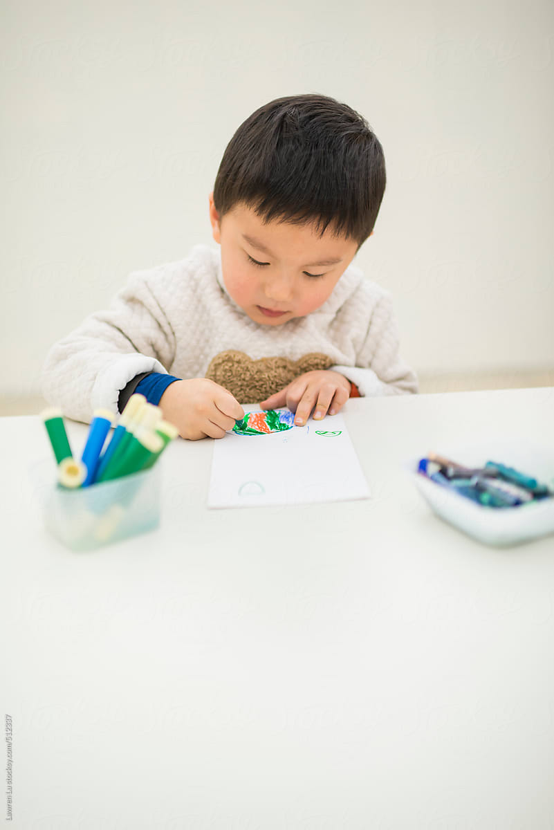 Chinese Kid Coloring a Paper at the Table