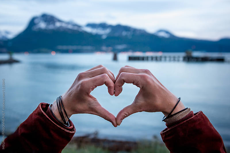 Female Hands in the Shape of a Heart with Seaside Sunset and Snowy Mountains