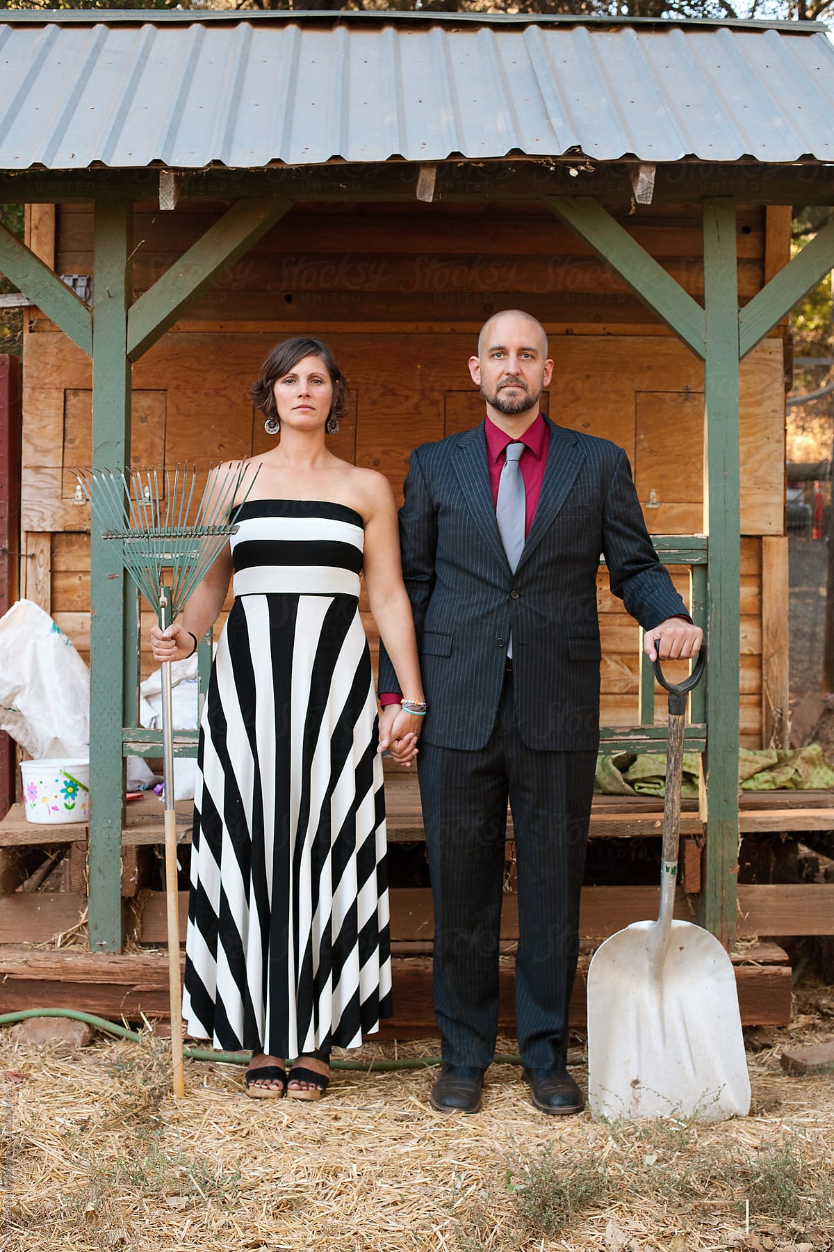 Woman and man in formal attire holding farm implements in front of chicken coop