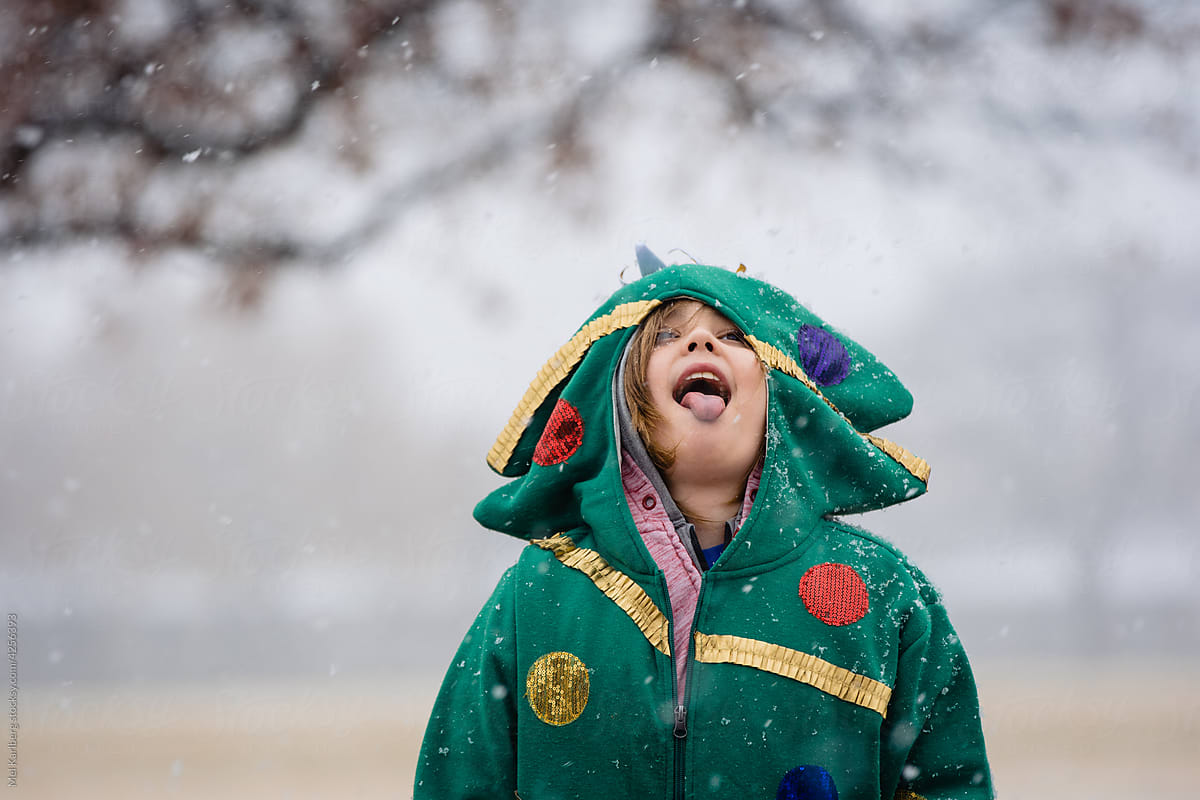 Boy in Christmas tree hoodie catching snowflakes 3