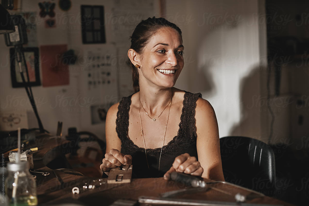 Smiling female jewelry maker sitting at her workbench