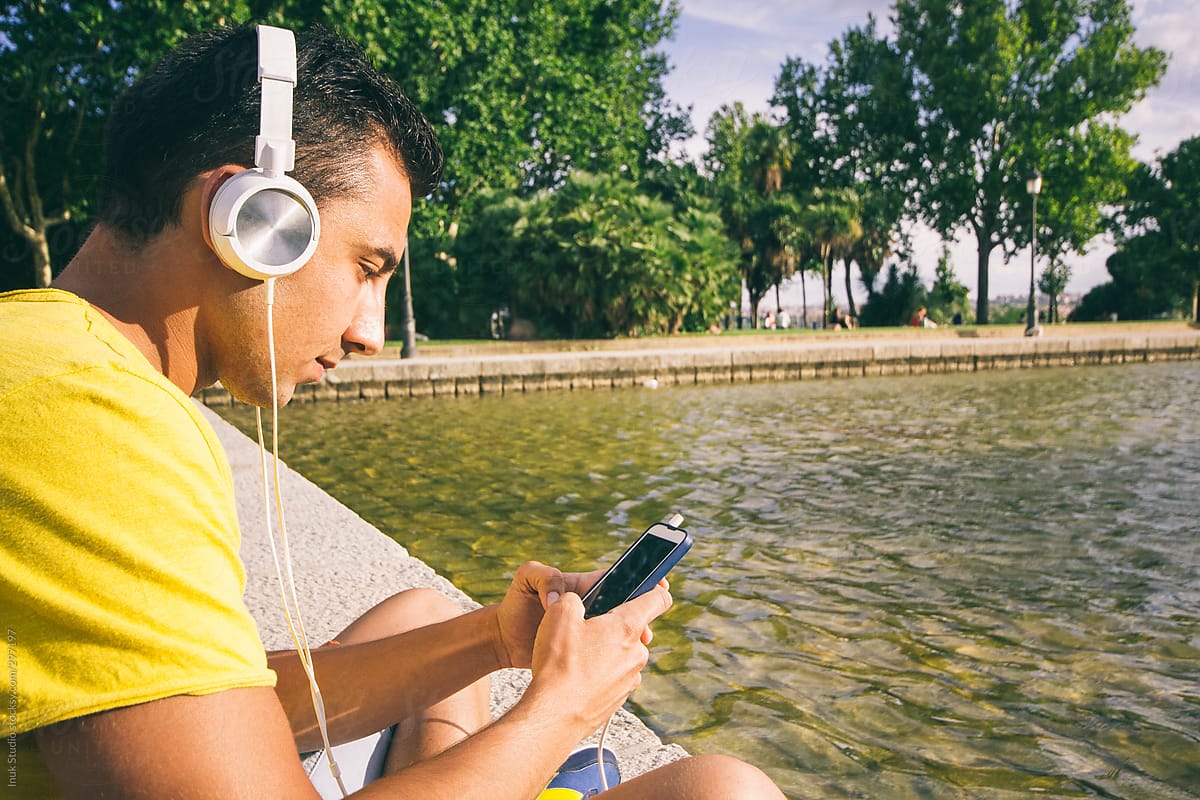Young man listening music with headphones near a park fountain