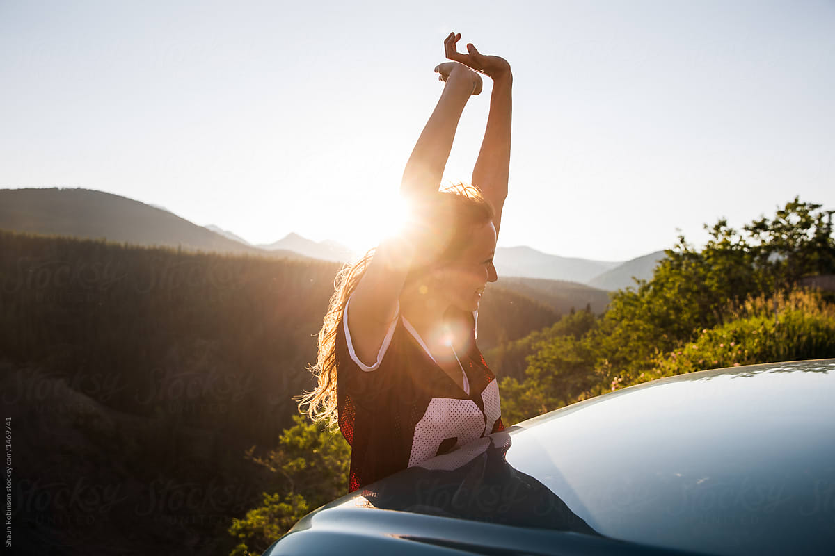 girl hanging out a car window with her hands in the air with the sun behind her