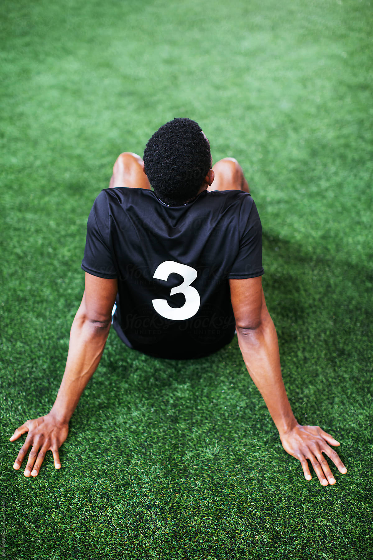 Back view of soccer player resting on football field.