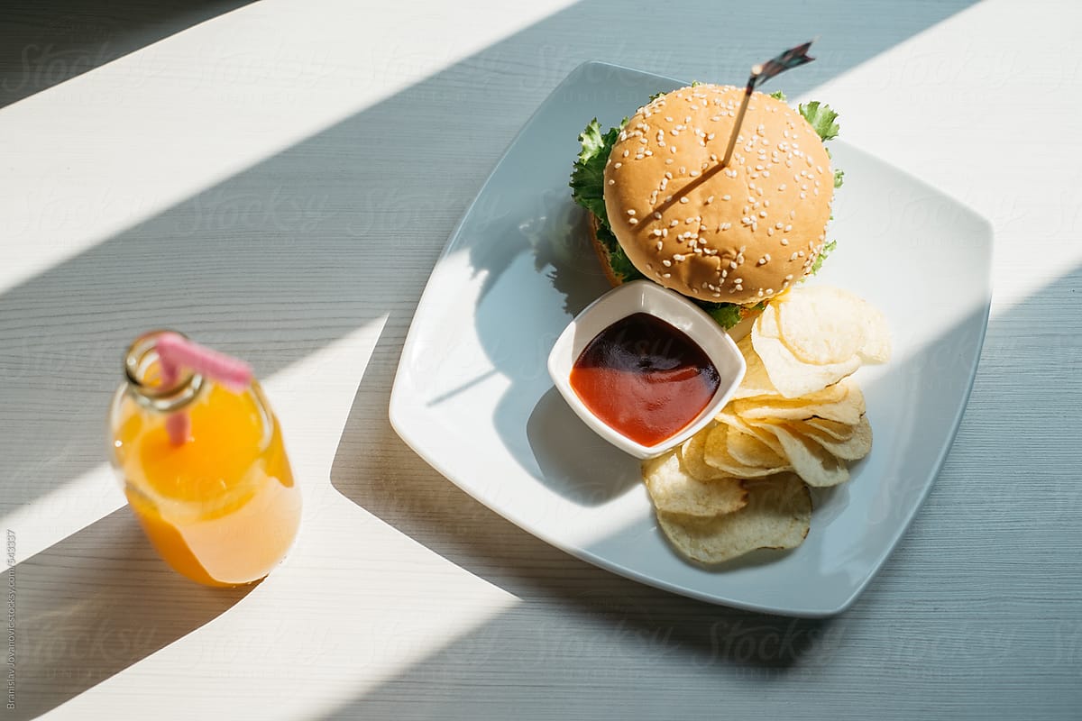 Burger Served With Chips And Orange Juice On The Table