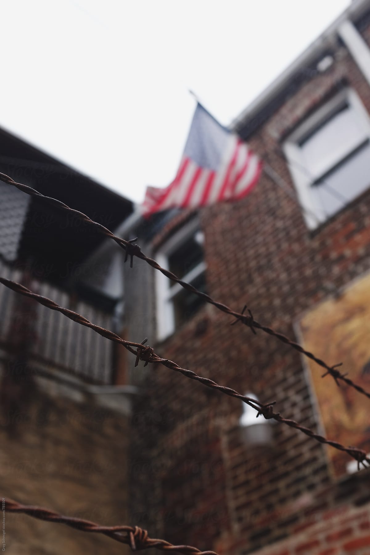 A barbed wire fence with an American flag waving in the background on a city building