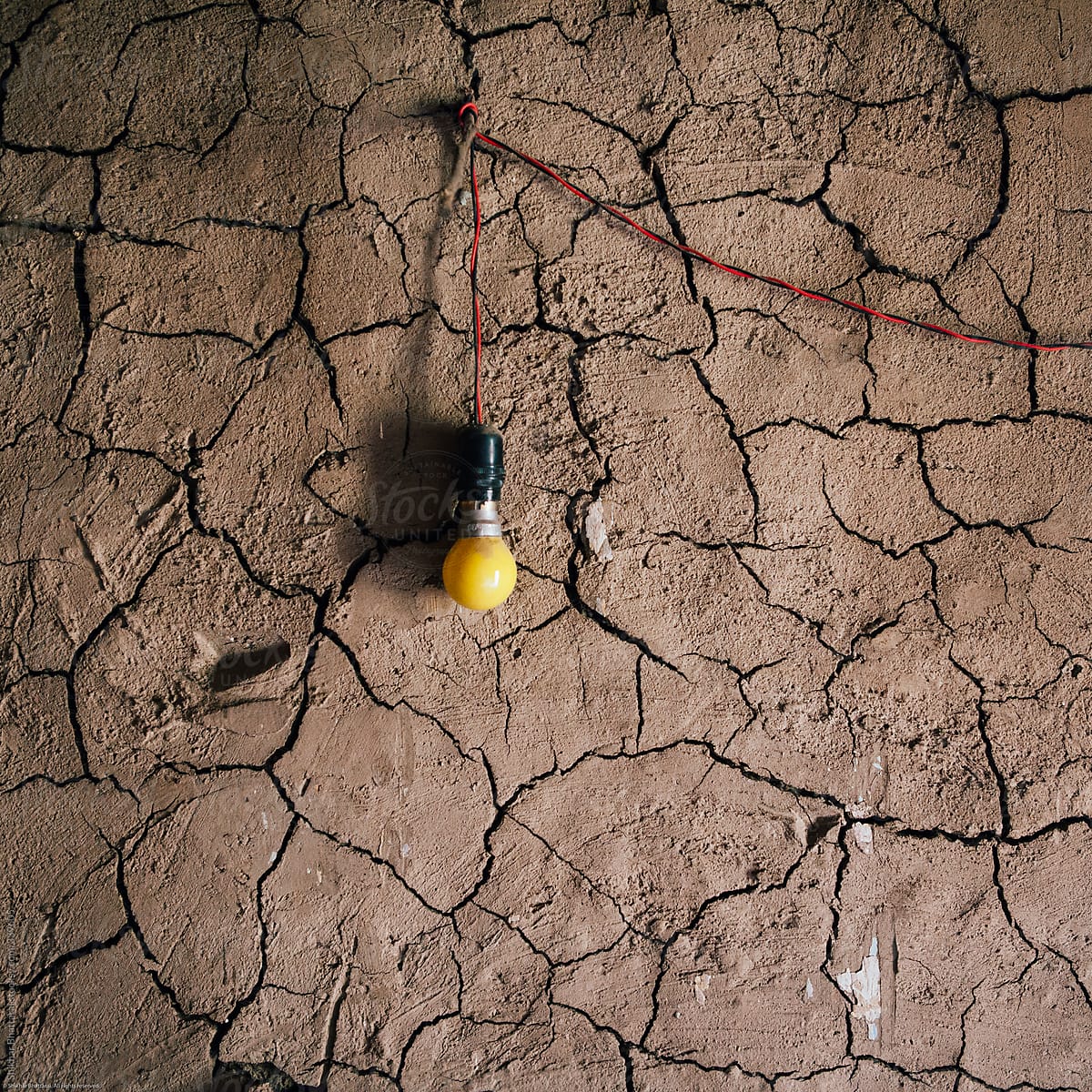 Abstract shot of light bulb on a cracked crumpled mud wall.