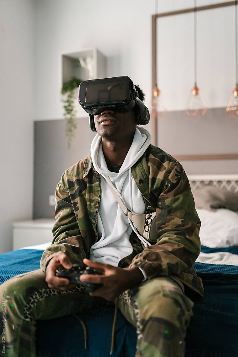 African American gamer sitting on bed and playing