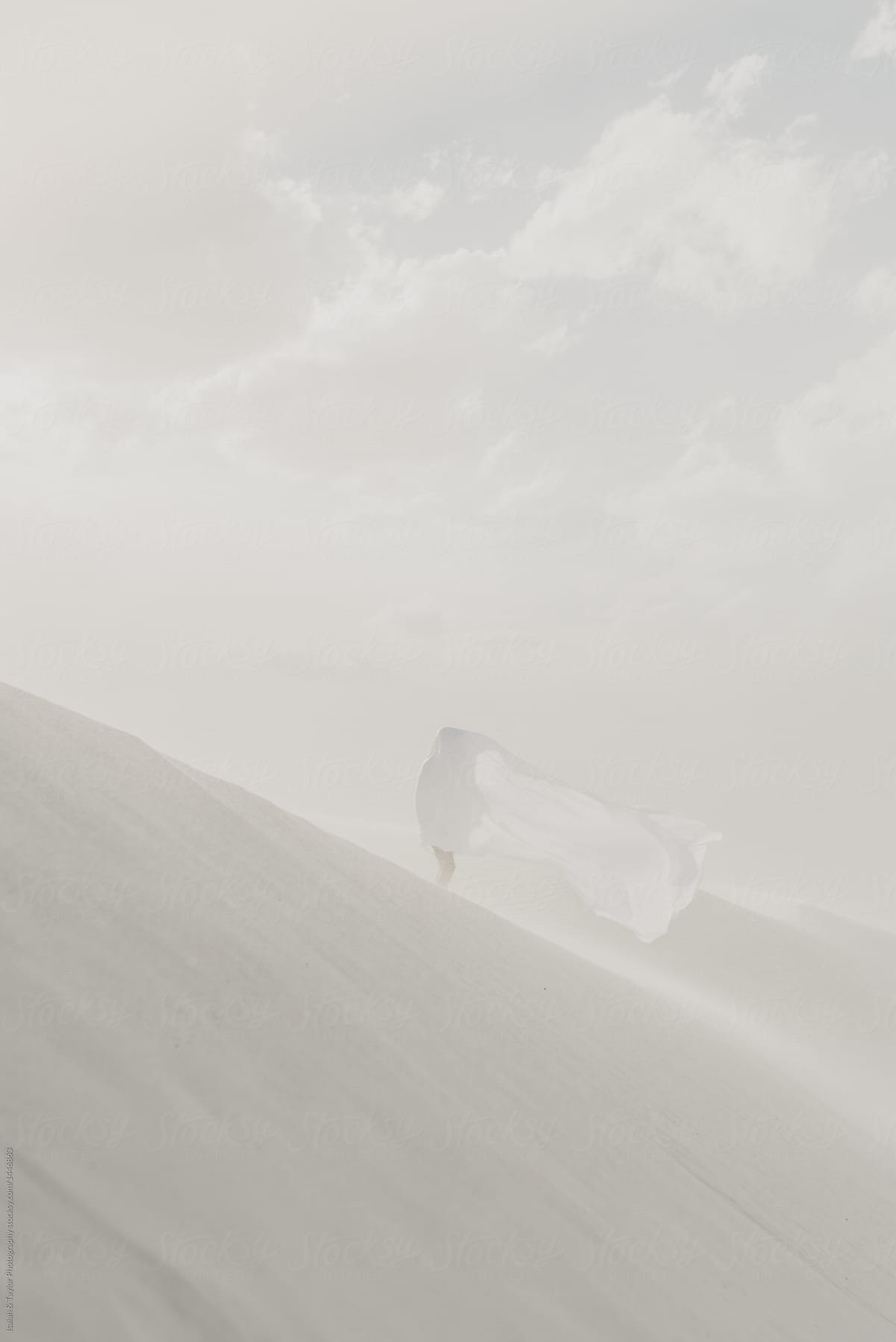 Person standing far away on sand dune with a white sheet disguising them into surrounding