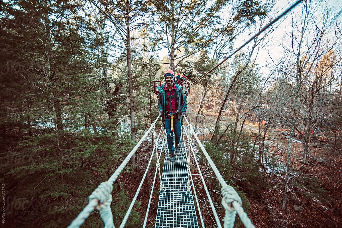 A young man walks across a bridge in the forest while zip lining