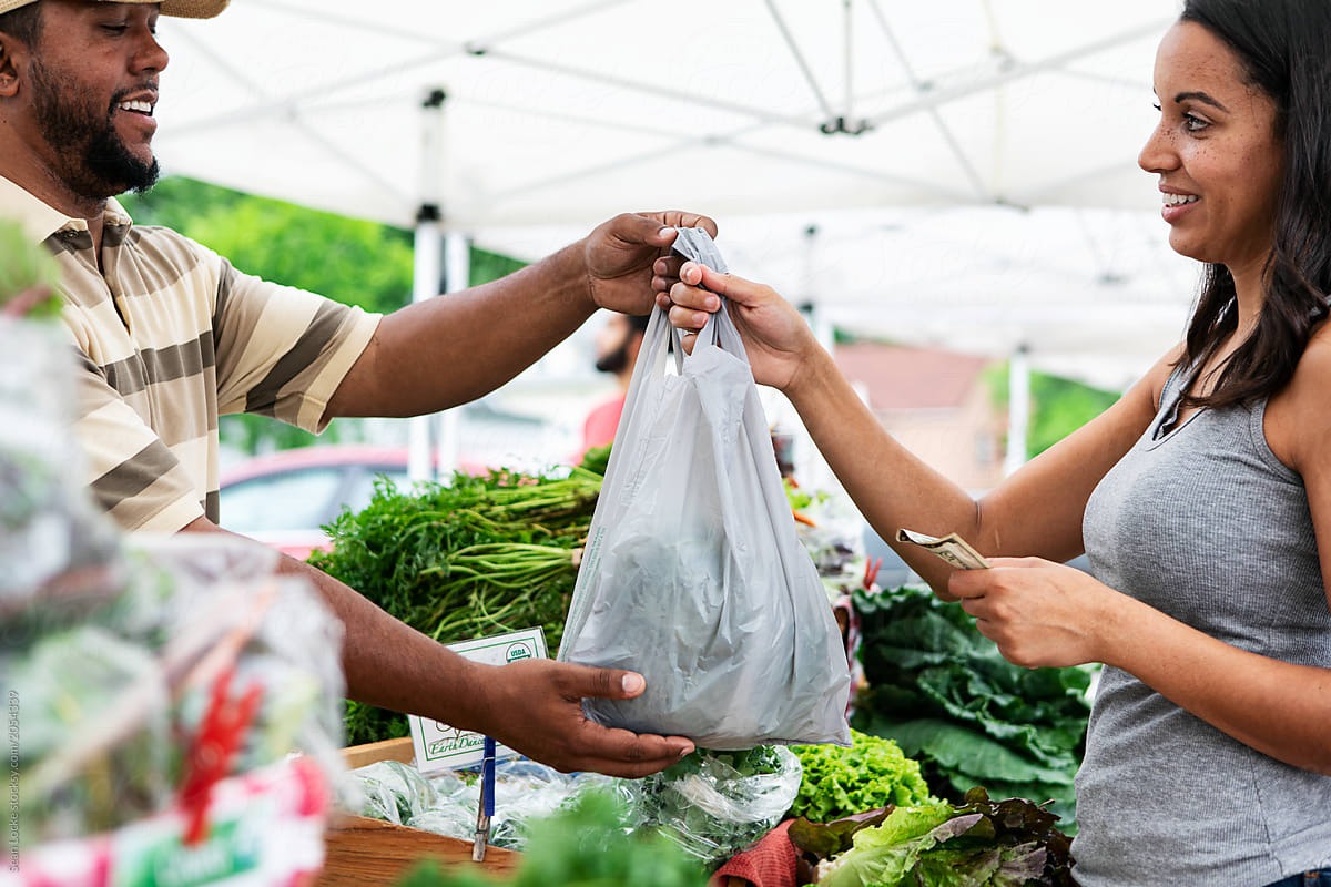Market: Farmer Hands Bag Of Produce To Customer
