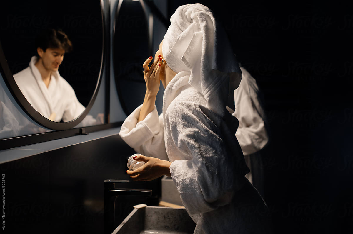 Woman in bathrobe putting face cream in bathroom