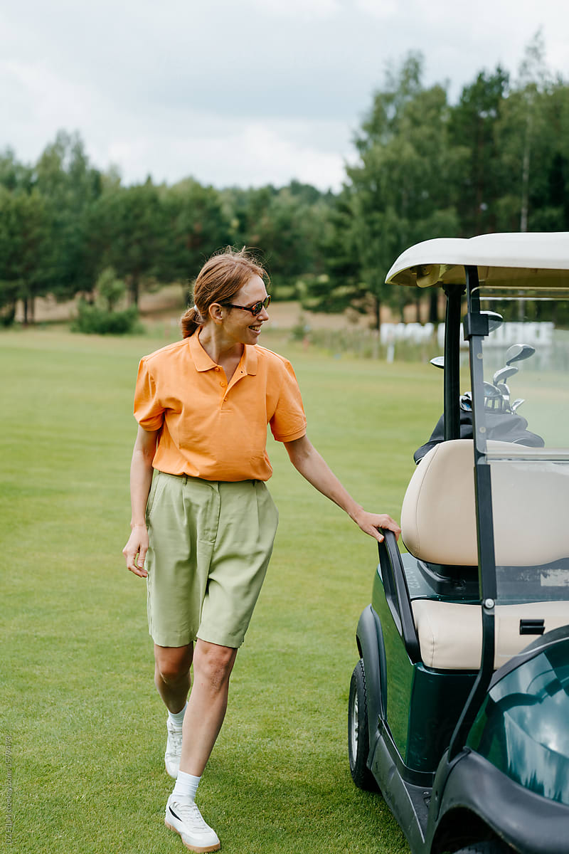 A woman smiles standing near a golf car on the course