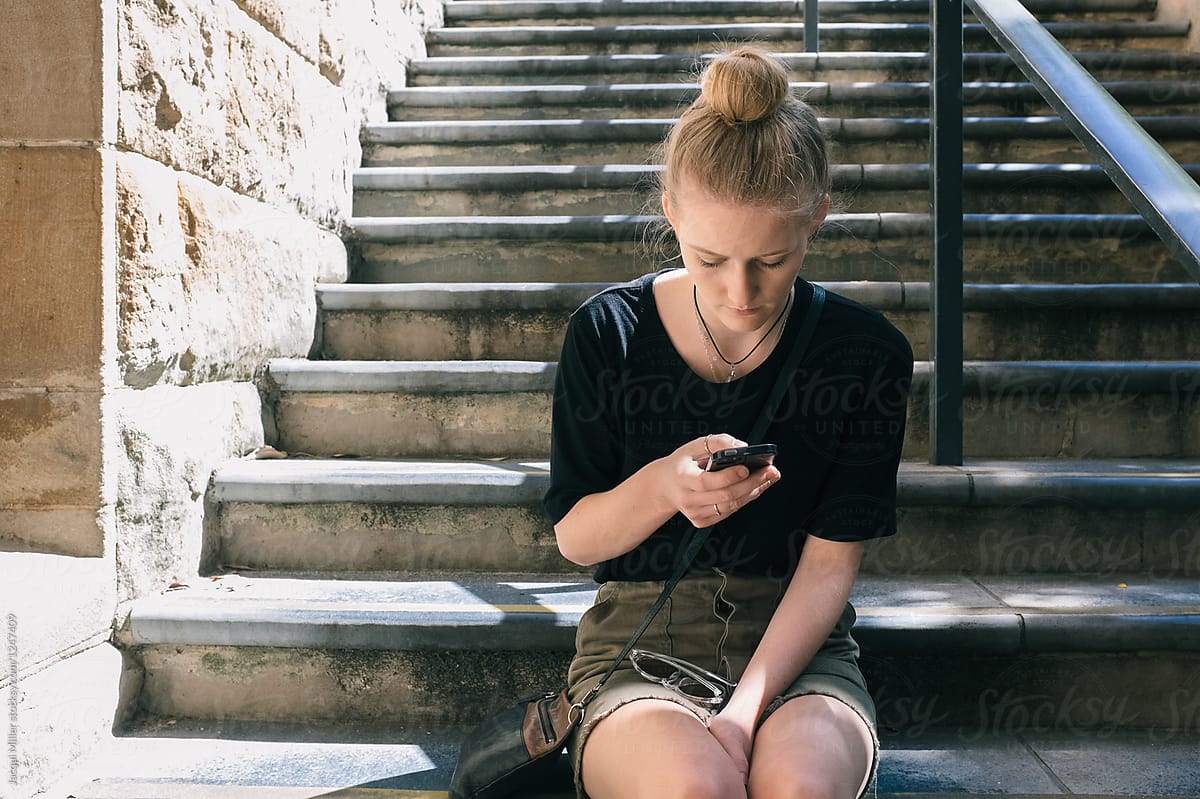Young woman, sitting on outdoor steps, using a cell phone
