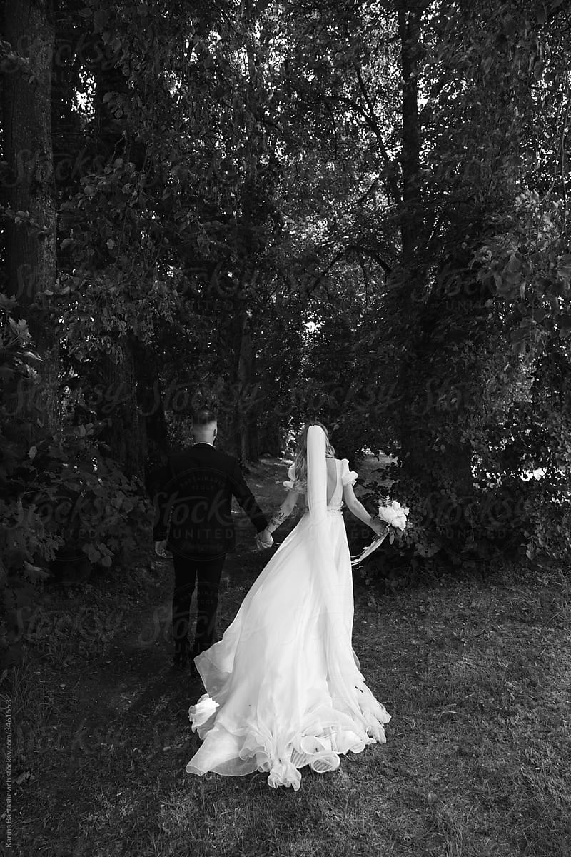 black and white photo of the bride and groom walking after the wedding in the forest