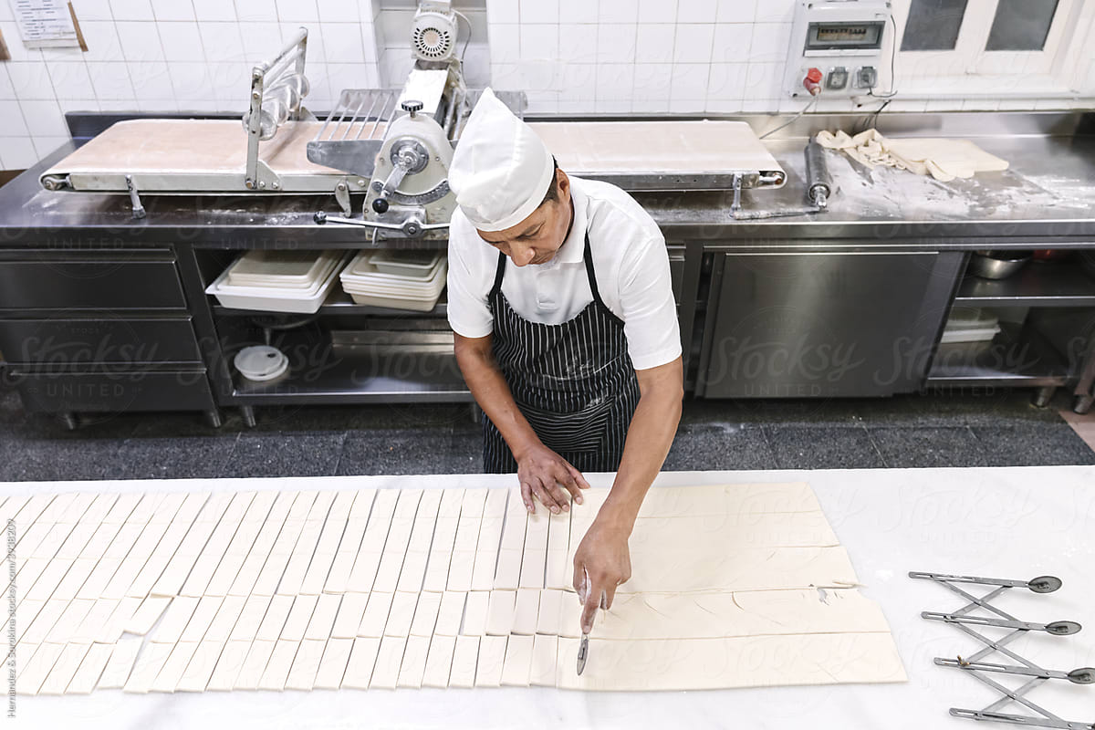 Worker At Bakery Cutting Dough