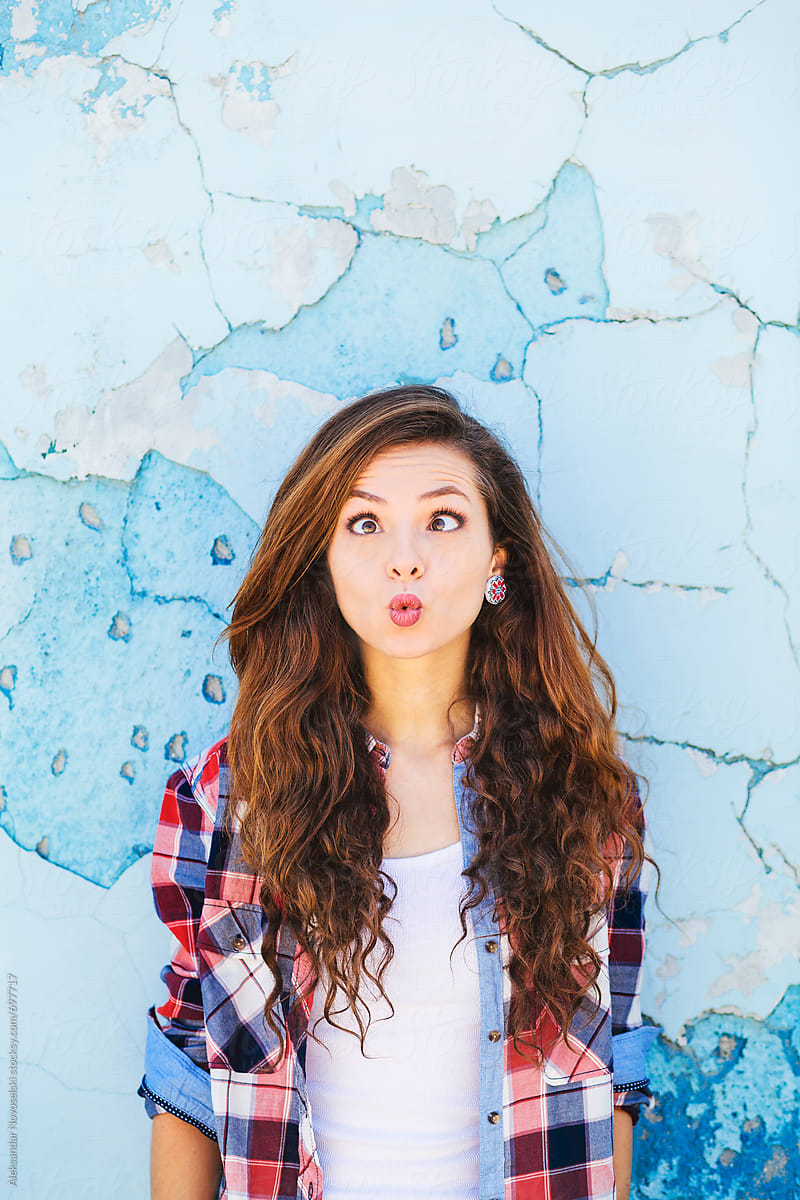 Cute Girl Making Funny Faces Against A Blue Wall By Aleksandar Novoselski