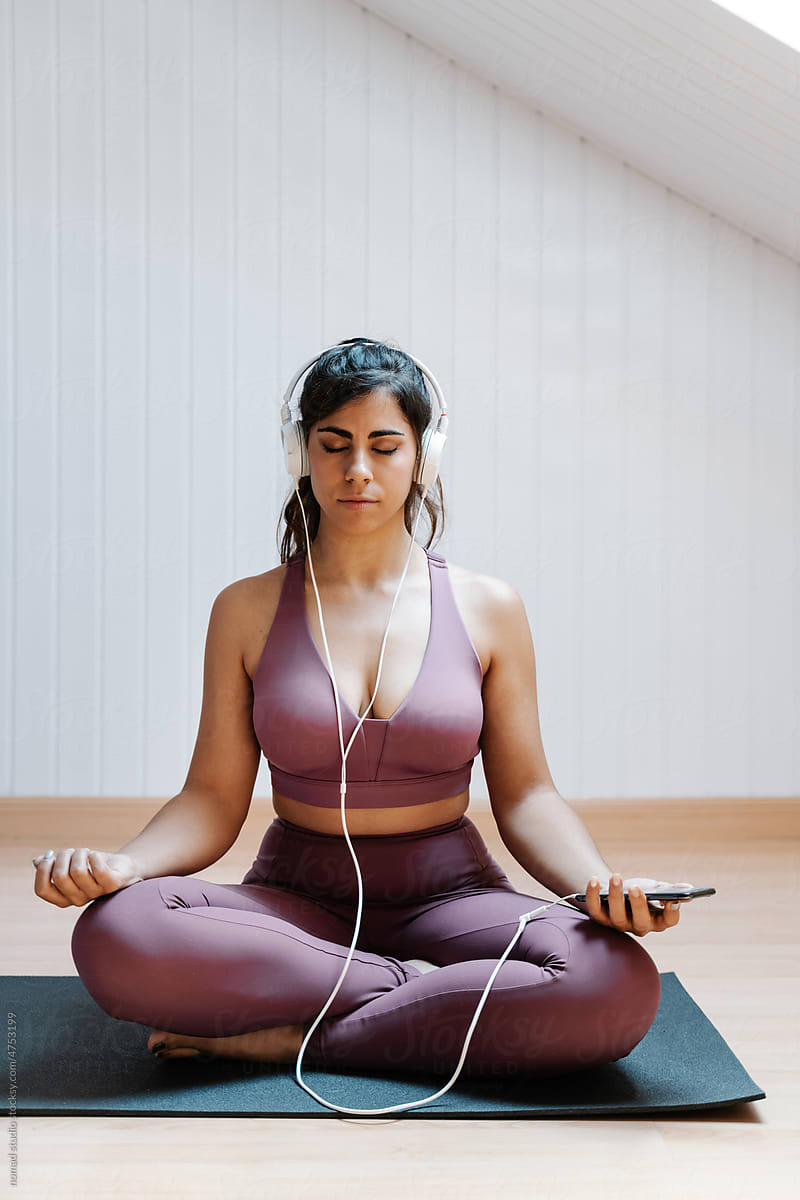 Young woman with smartphone and headphones meditating at home