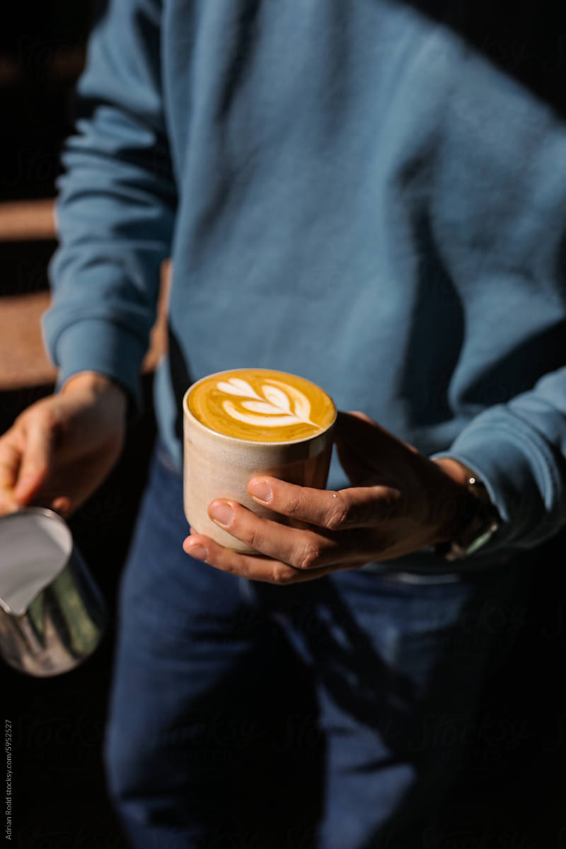 A barista holding a freshly made flat white specialty coffee