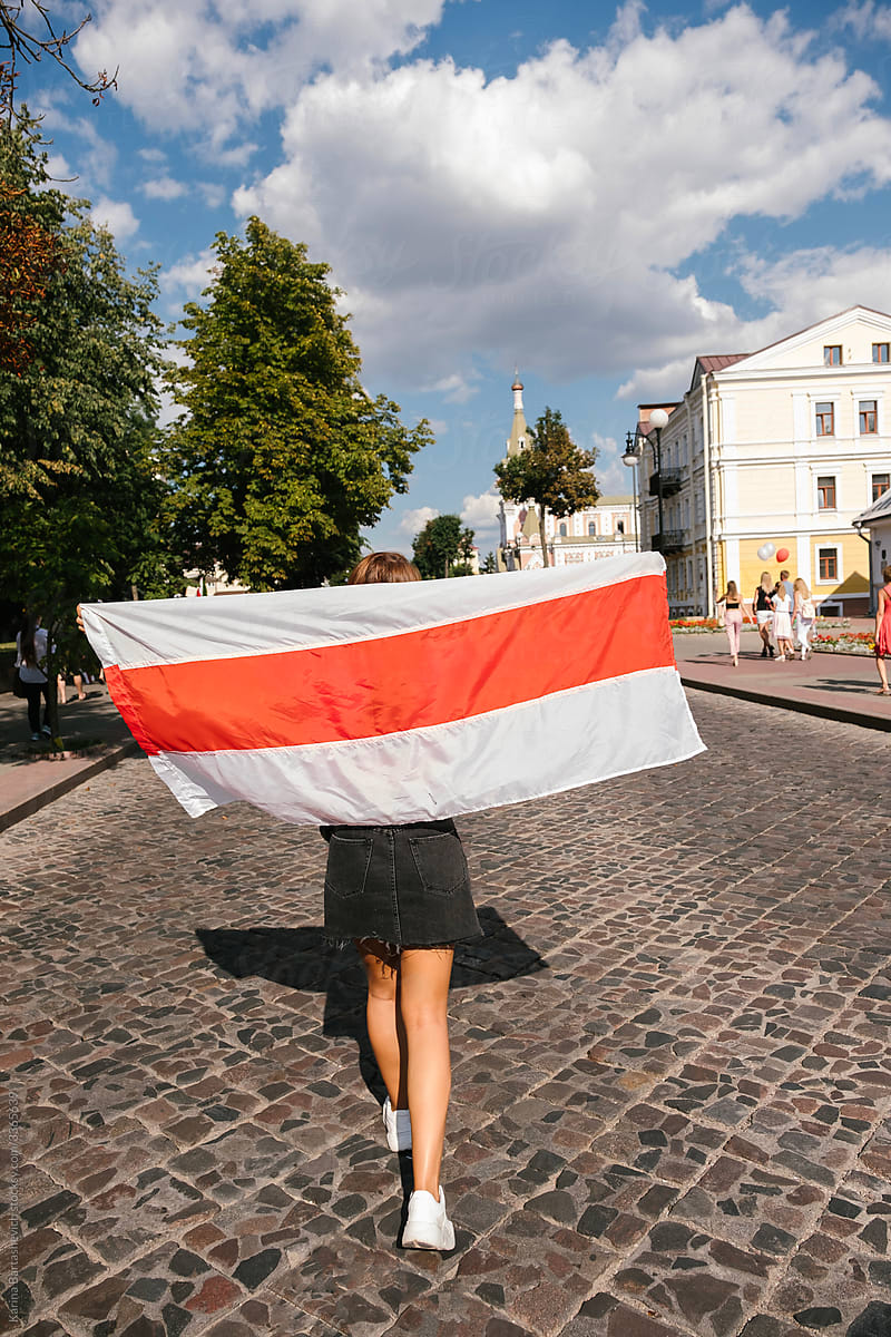 a girl at a peaceful protest carries a red and white flag, stretching it out behind her back