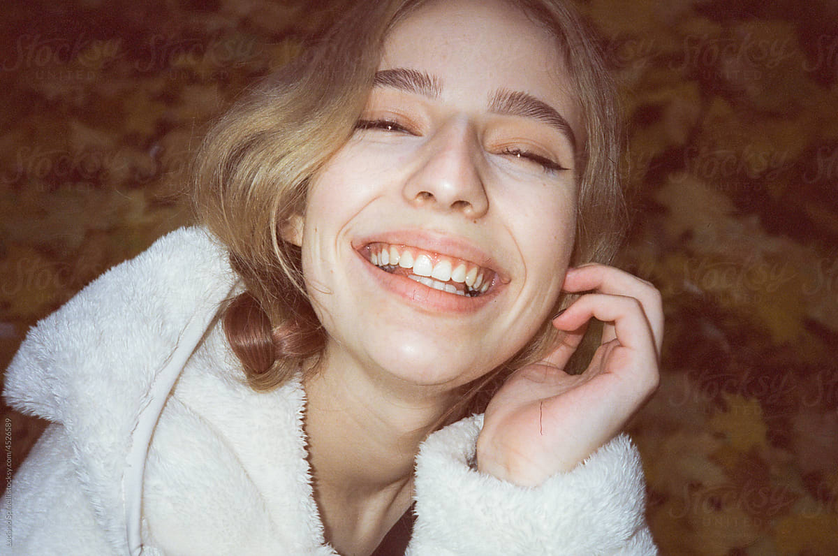 Blond girl laughing with closed eyes wearing a white hoodie