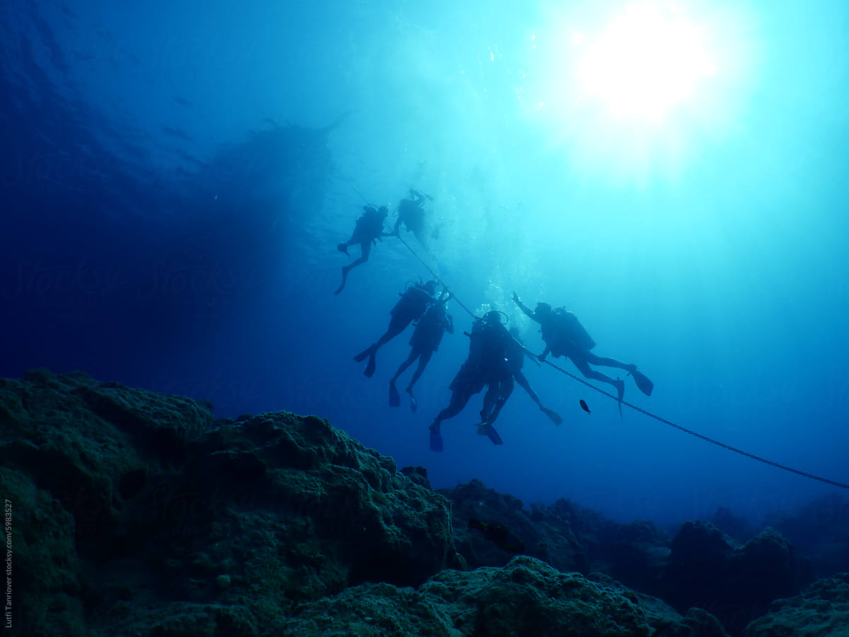 scuba divers holding on boat rope underwater