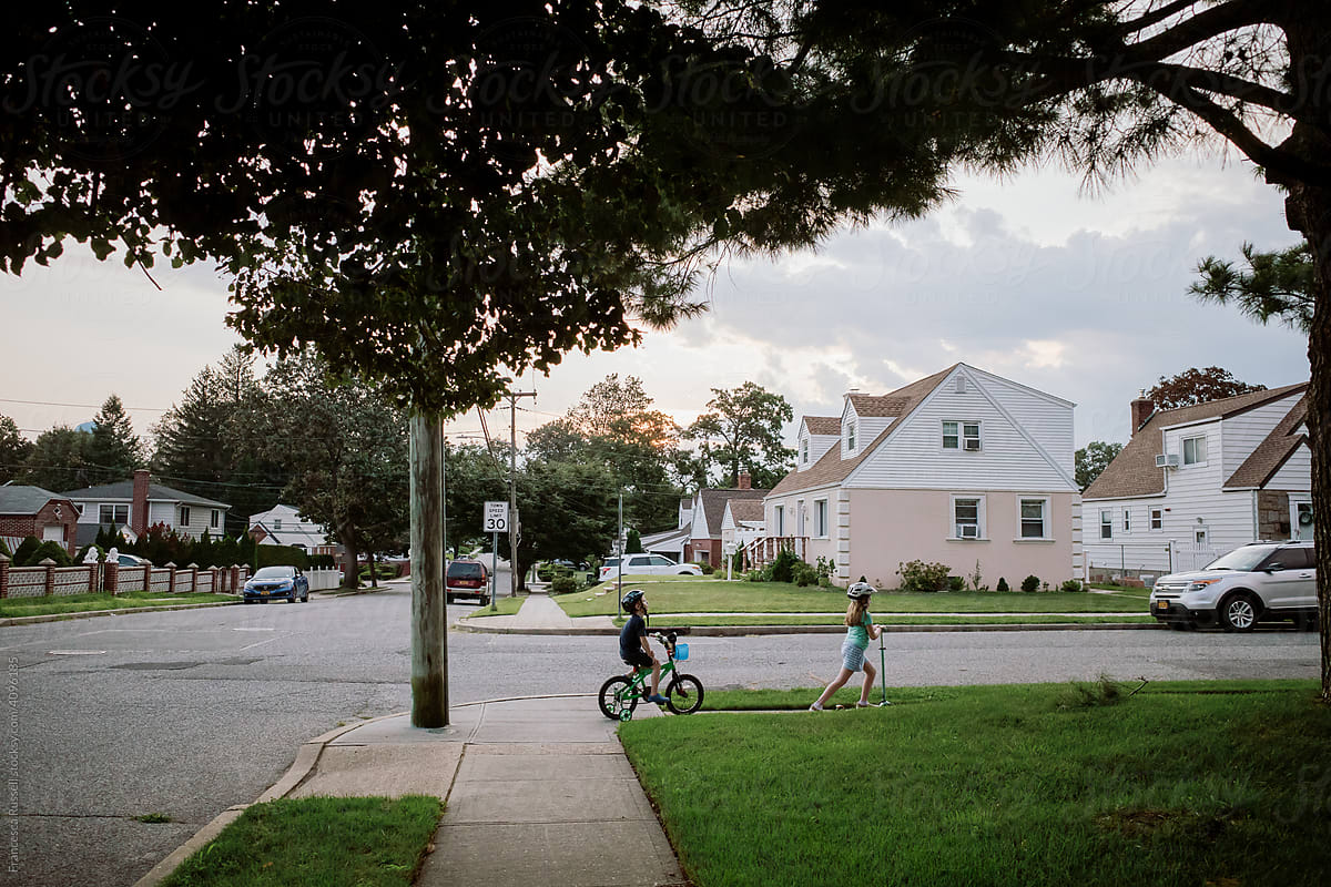 Two children ride scooters down a suburban street.