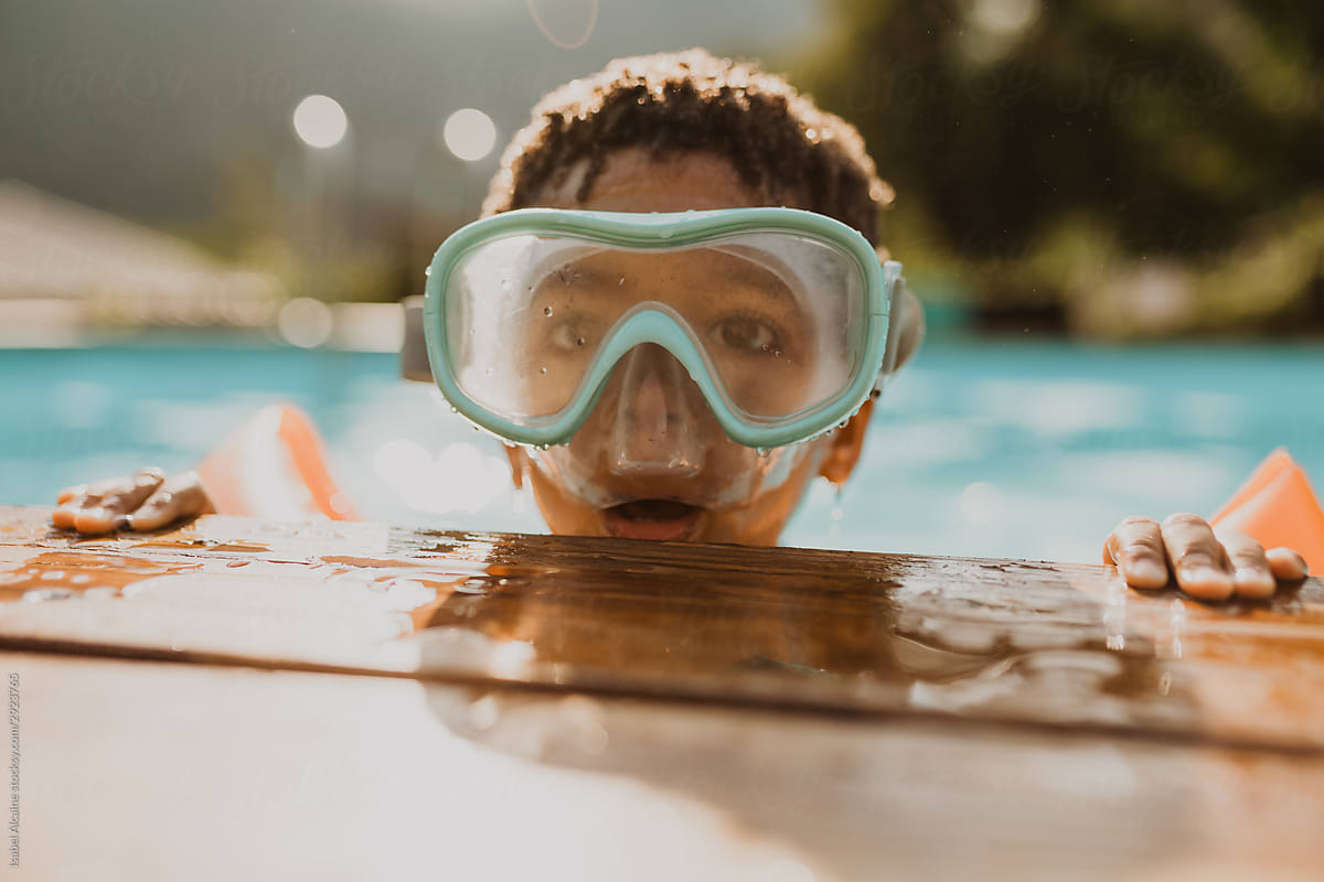 African American boy in a pool with blue diving goggles and orange muffs
