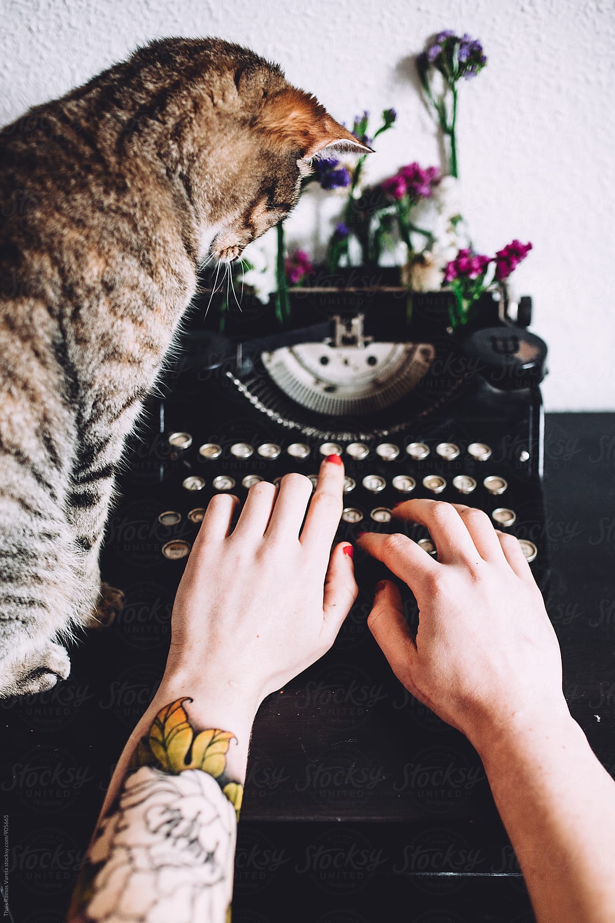 Woman typing in a vintage typewriter with flowers and a cat