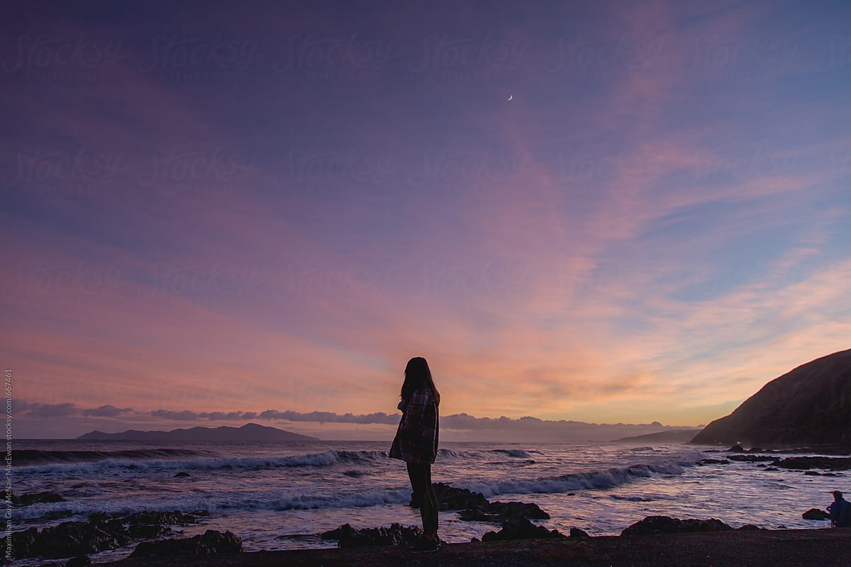 Silhouette of a young woman standing on the coast at dawn