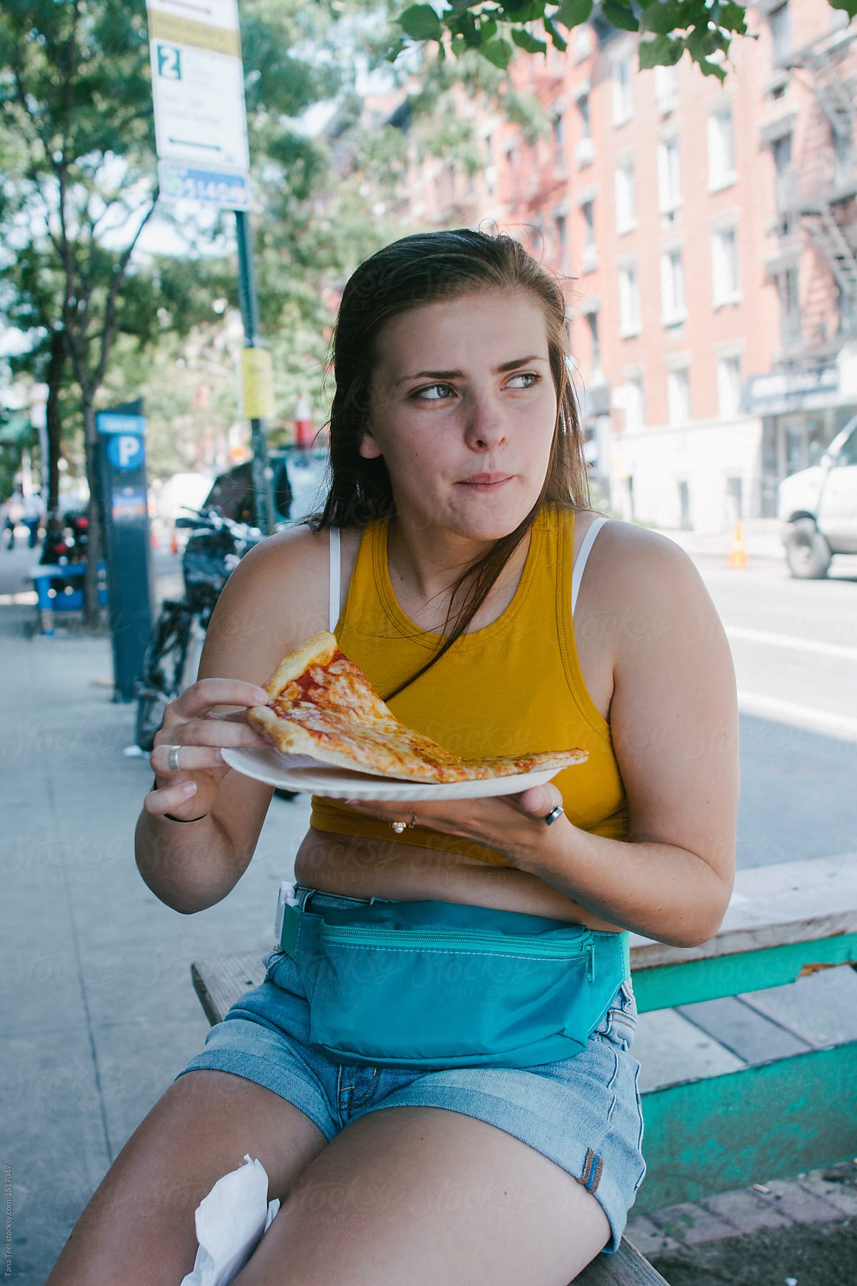 teenager eating a slice of New York pizza on summer day