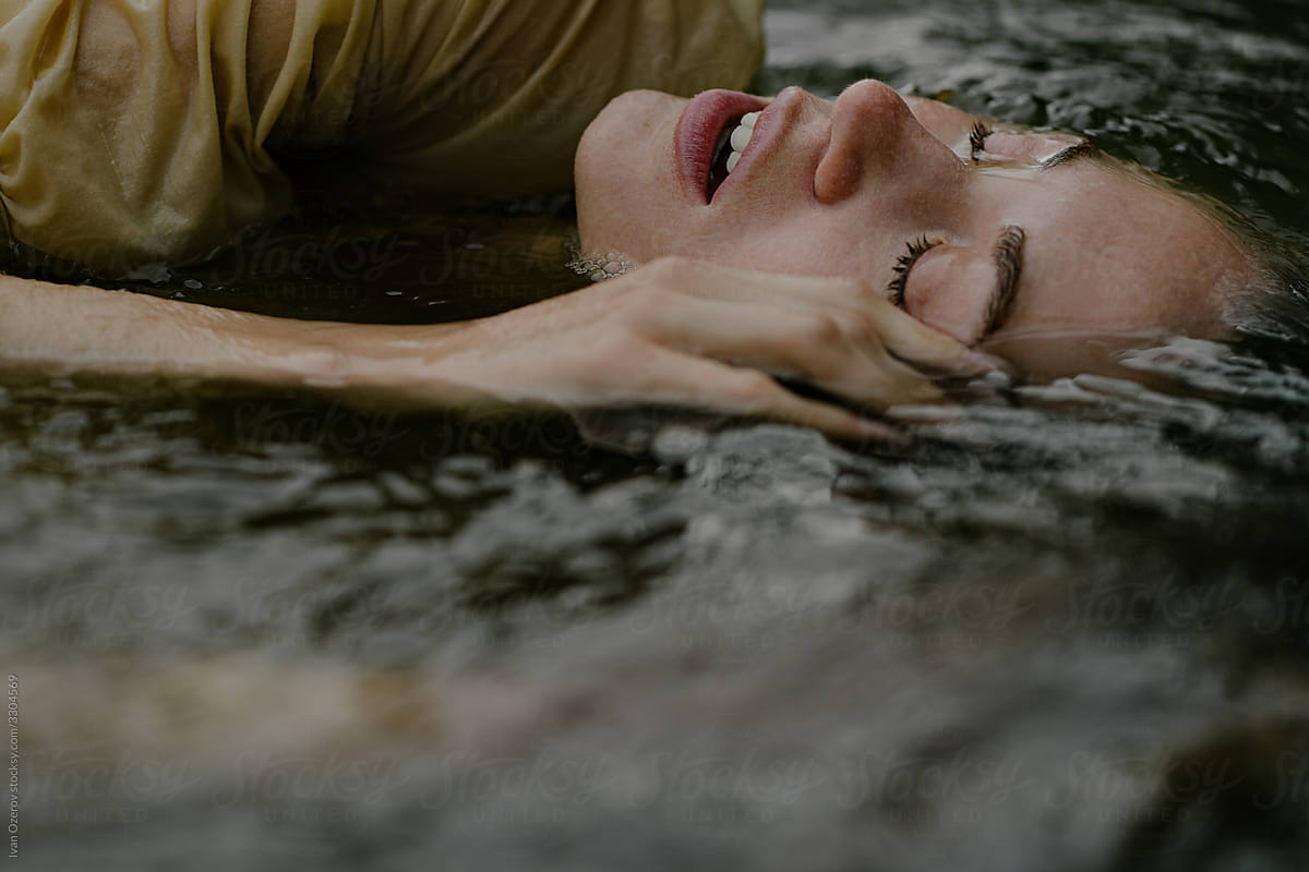 beautiful young-eyed woman lies in the water with closed eyes and open lips