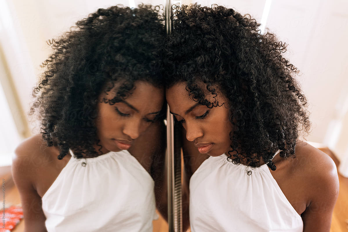Young African American woman sitting on floor near big mirror with reflection in apartment