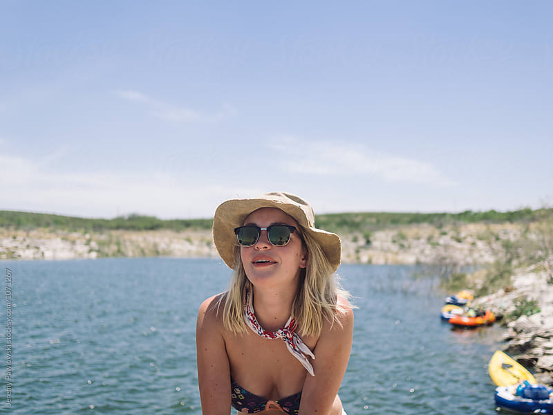 Hip young woman wearing bucket hat and sunglasses sitting near sunny lake