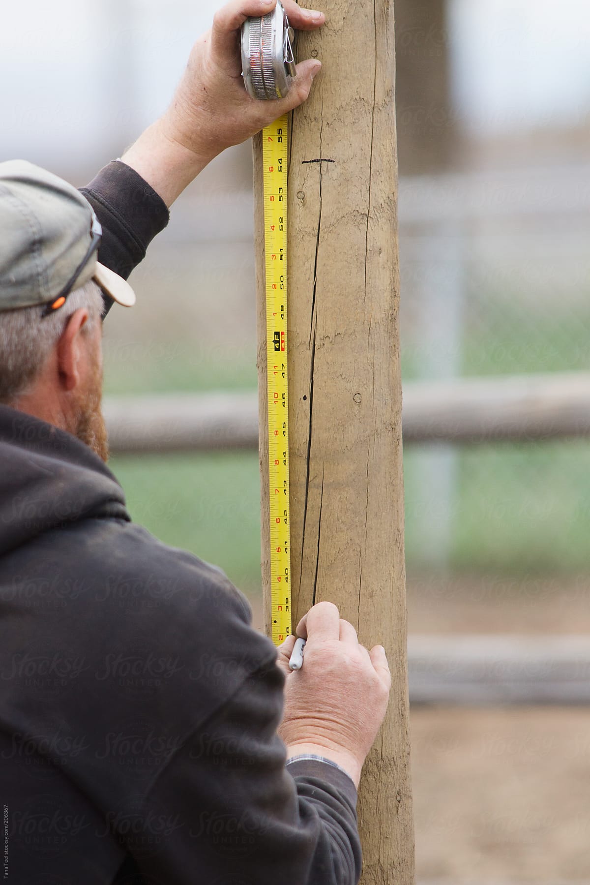 Man uses measuring tape to measure a fence post