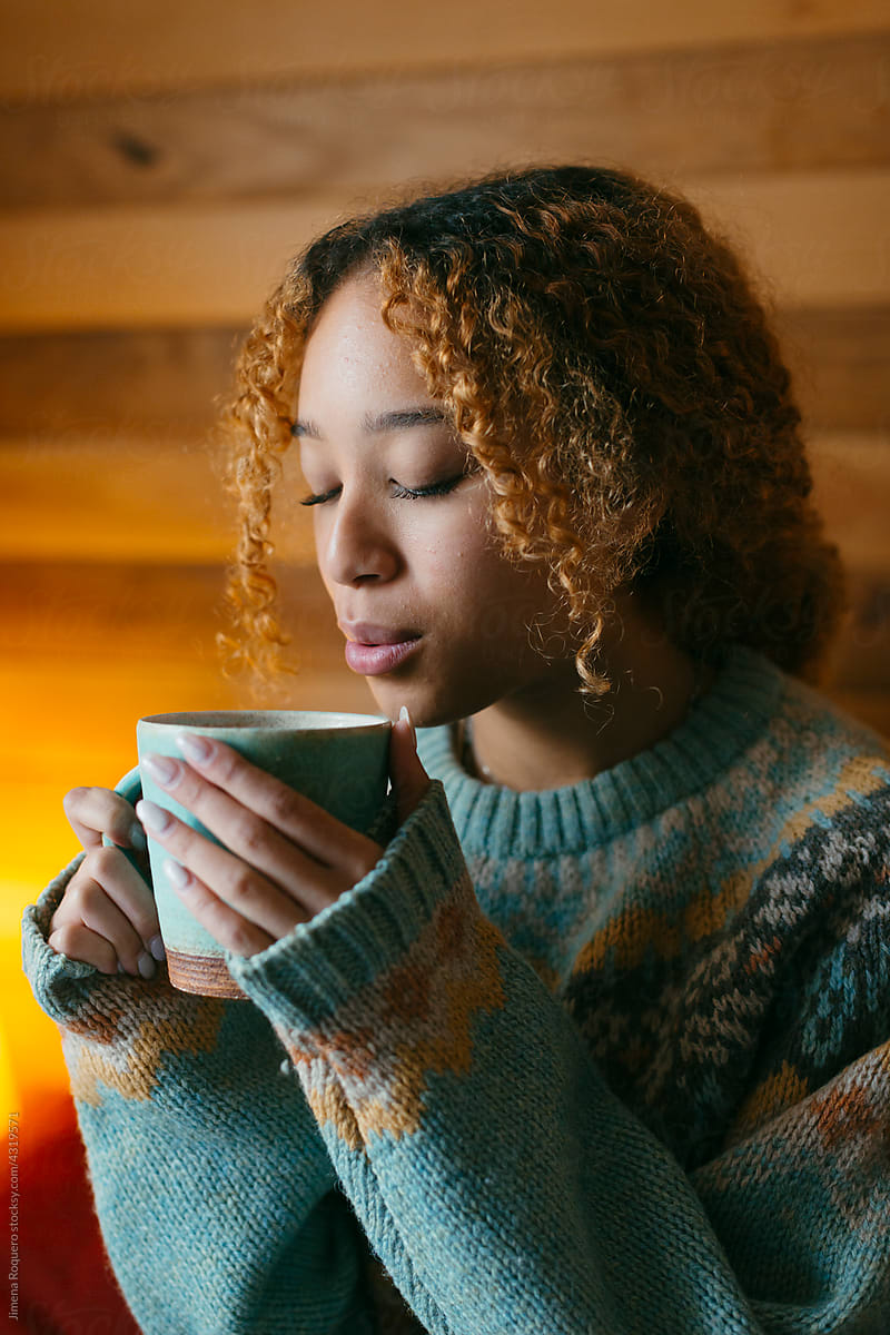 Young woman drinking hot tea in cozy bedroom