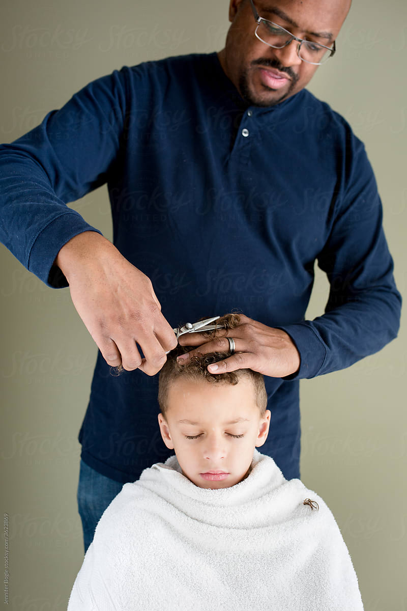 Father carefully trims boy\'s hair at home