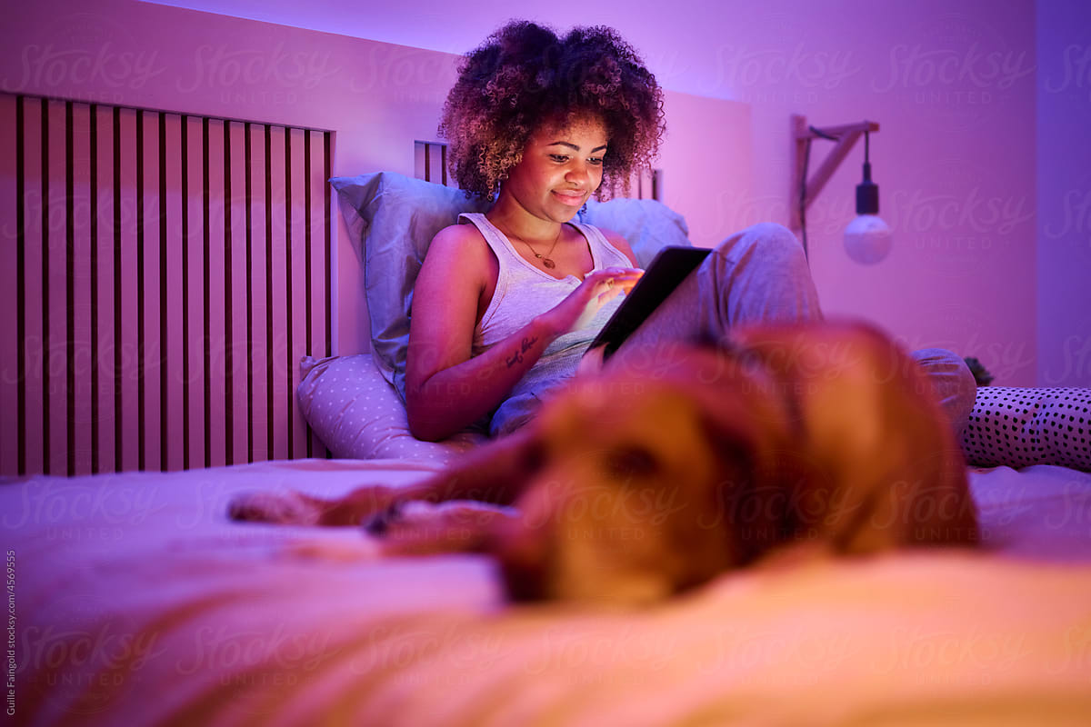 Student surfing Net on tablet on her bed with pet.