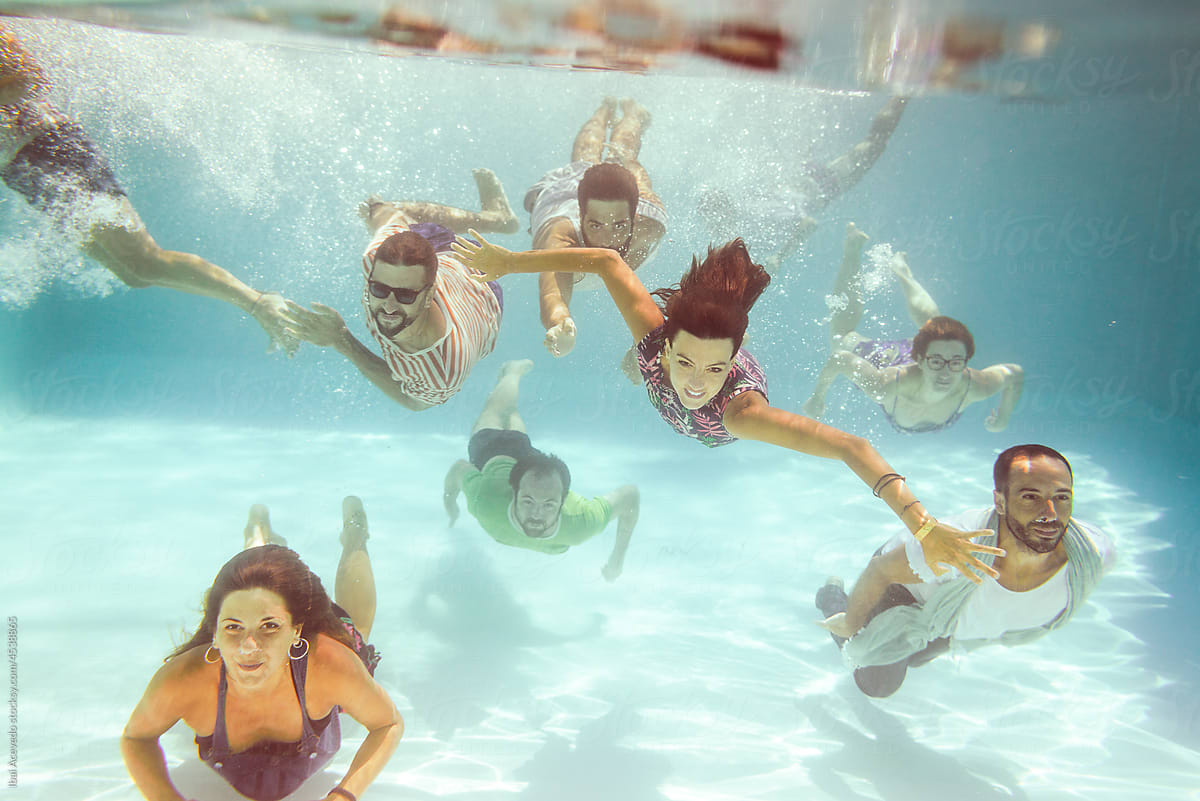 Cheerful dressed friends diving inside swimming pool