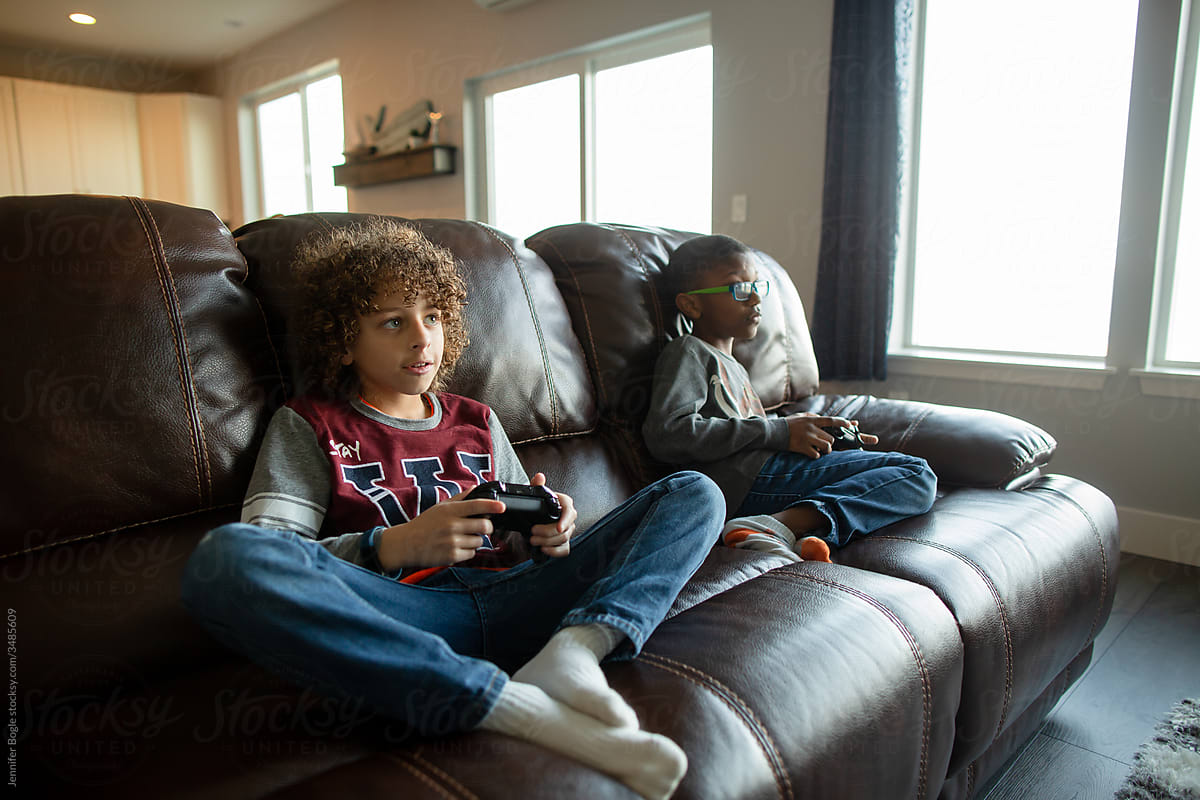 Boys lounge on leather couch playing video games