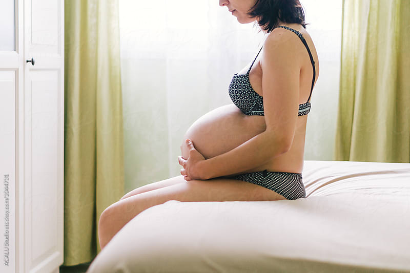 Pregnant woman sitting in bed touching her belly