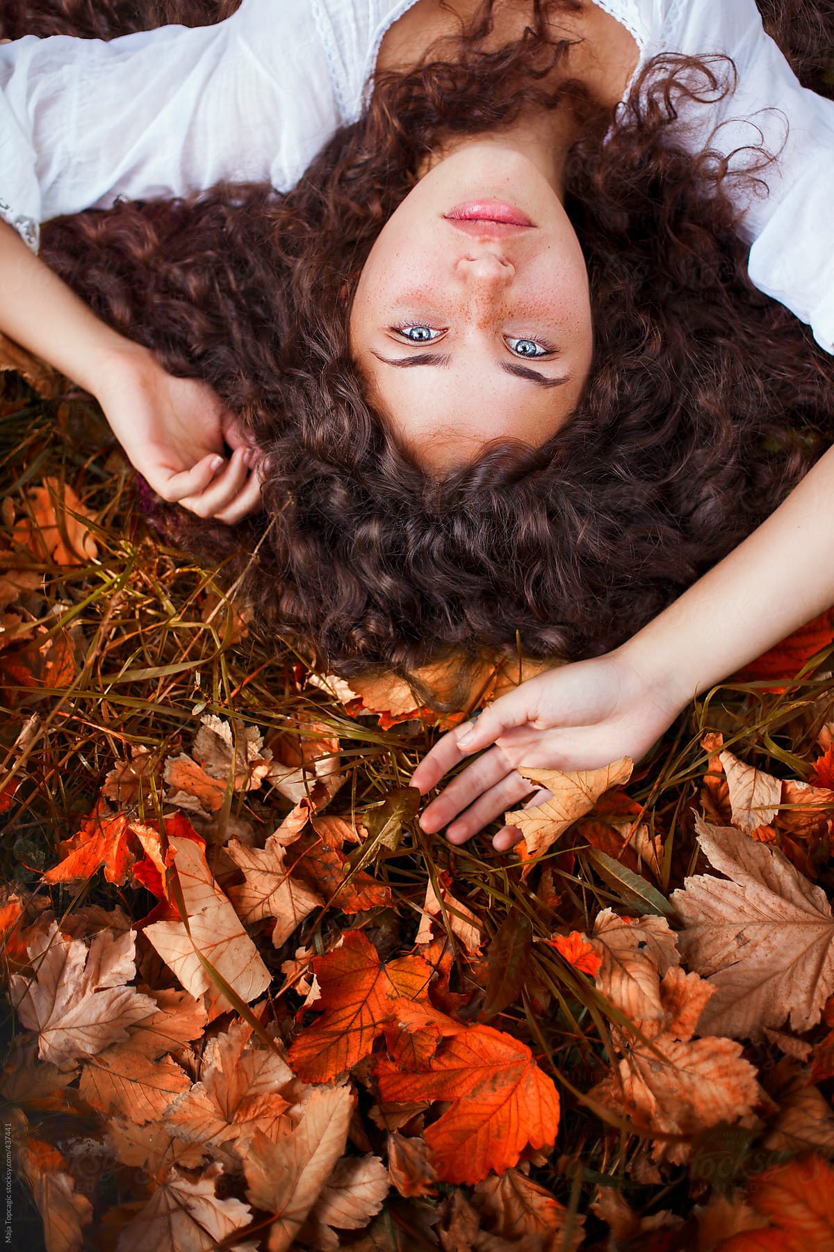 Beautiful young woman with curly hair, blue eyes and freckles lying on the leaves