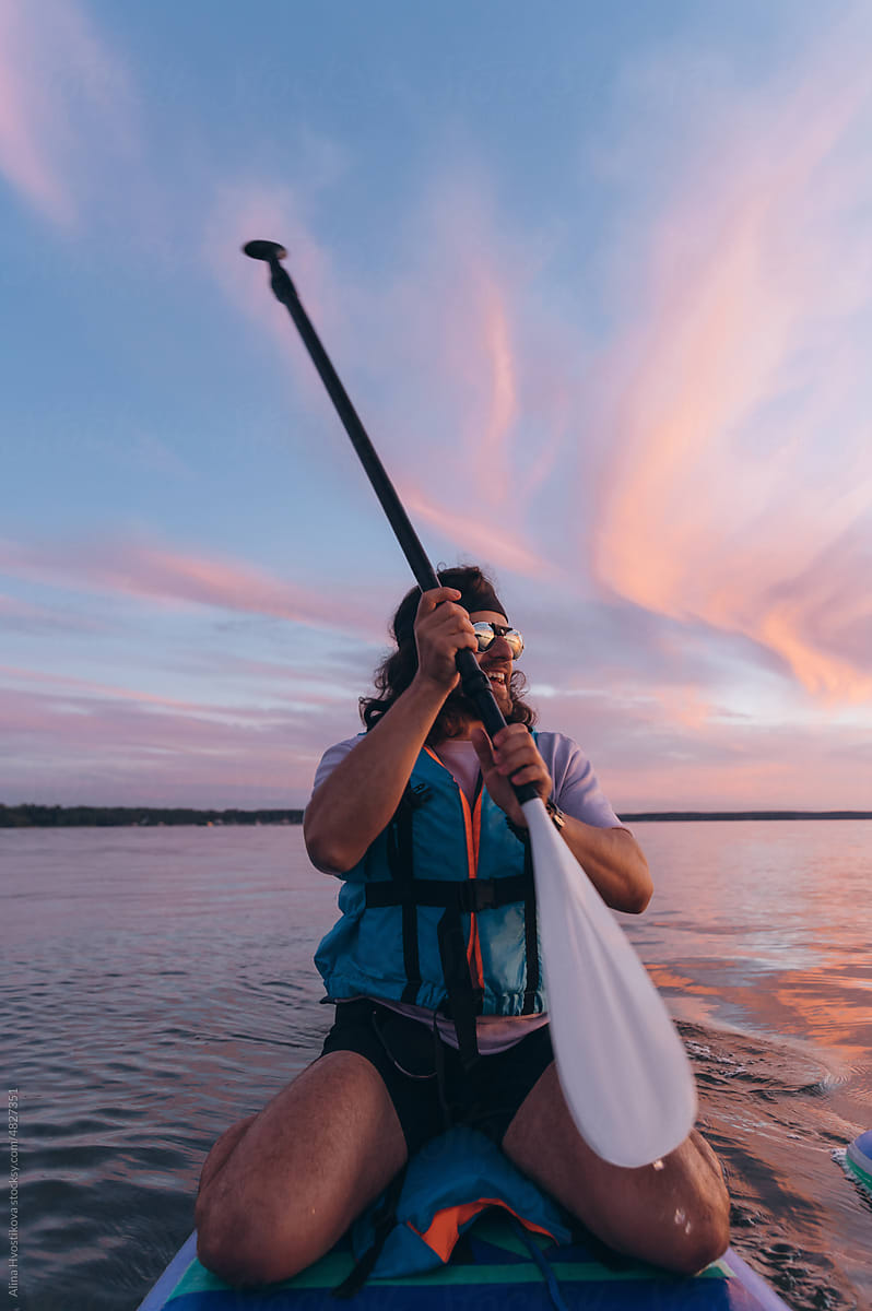 Young guy using smartphone on paddleboard at sundown