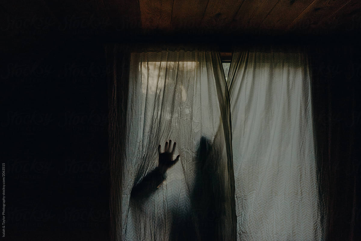 A shadowed silhouette of a person hiding behind a curtain reaching hand out against surface