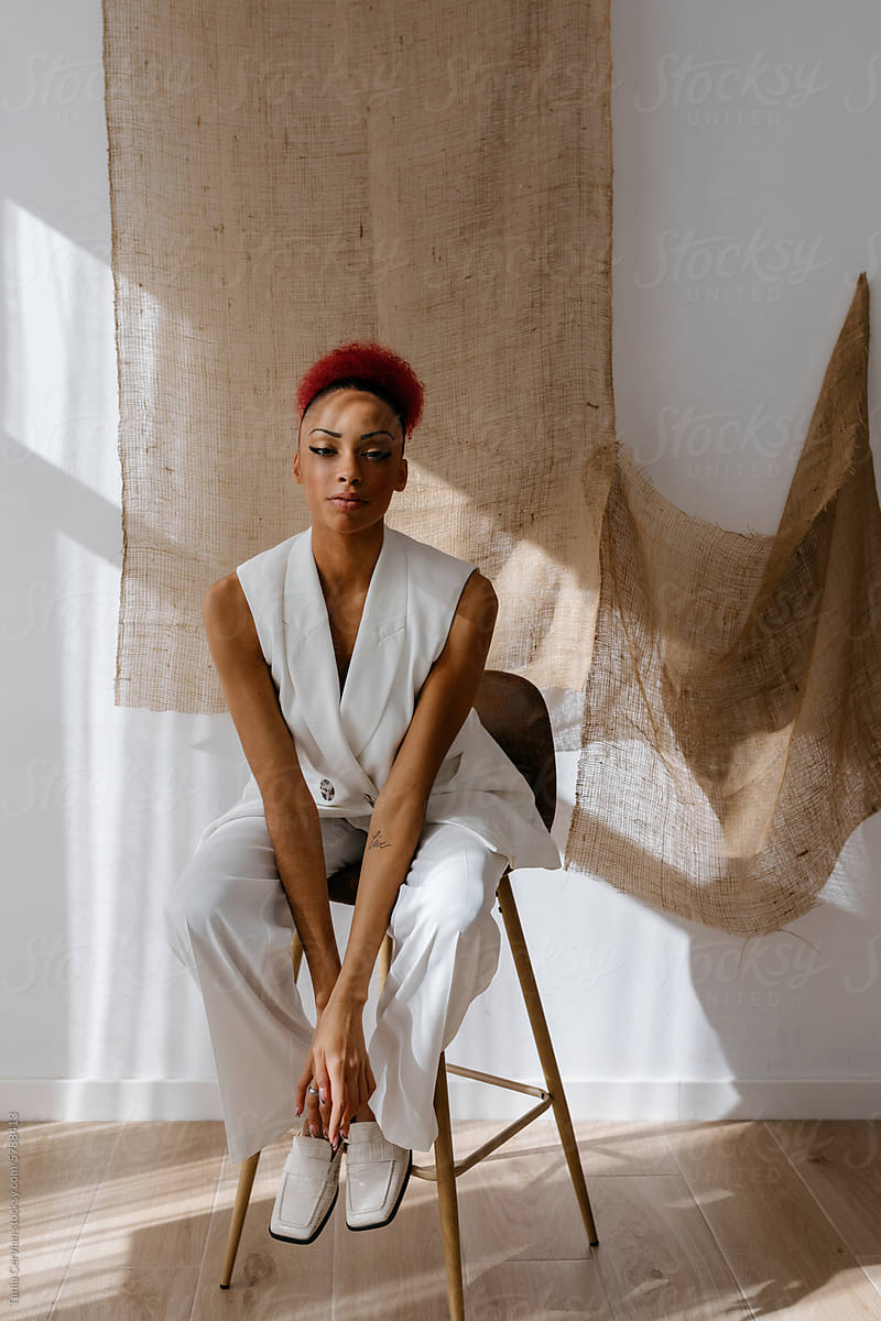 Stylish African American young woman sitting on stool chair in studio